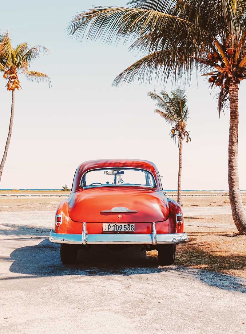 orange car parked on the beach in Havana by palm trees